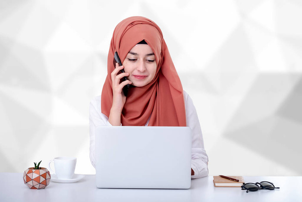 Muszlim nő dolgozik számítógéppel, hidzsáb muzulmán lány az irodában, és ő beszél a mobiltelefonon, támogatás, kapcsolat vagy ügyfélszolgálati koncepció fotó - Fotó, kép