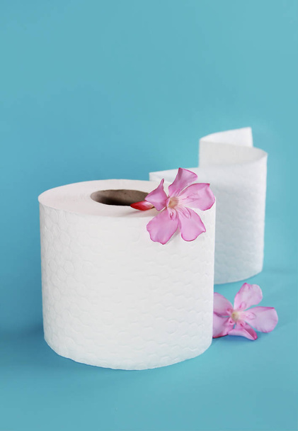 λευκό ρολό χαρτί τουαλέτας με λουλούδια διακόσμηση σε μπλε φόντο - Φωτογραφία, εικόνα