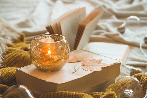 Γλυκό σπίτι. Λεπτομέρειες ζωής στο εσωτερικό του σαλονιού. Πουλόβερ και κερί, φθινοπωρινή διακόσμηση στα βιβλία.  - Φωτογραφία, εικόνα