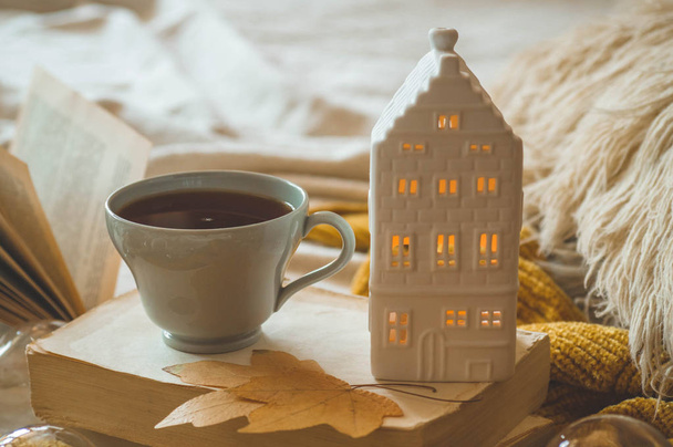Stillleben Details im Wohnbereich des Wohnzimmers. Pullover und Tasse Tee mit Kerzenhaus und Herbstdekor auf den Büchern - Foto, Bild