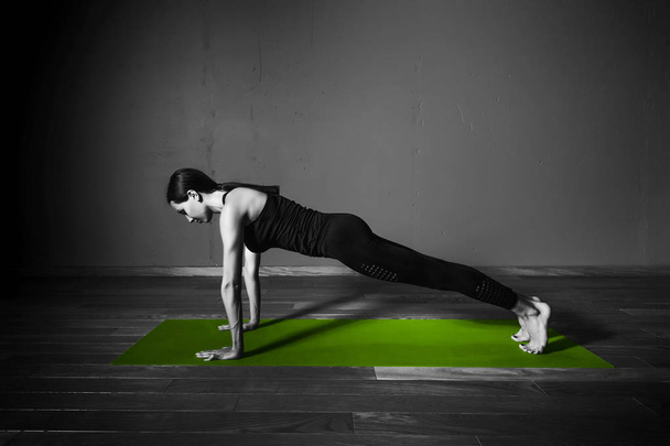 Black white photo of Young beautiful woman brunette in black clothes practice yoga kumbhakasana in dark studio green mat Sport meditation monochrome - Zdjęcie, obraz