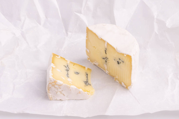 Голубой сыр с белой поверхностью, изолированный на белом фоне, мягкий свет, студийное фото, вид под углом. Смесь горгонзолы и сыра камамбер / бри
 - Фото, изображение