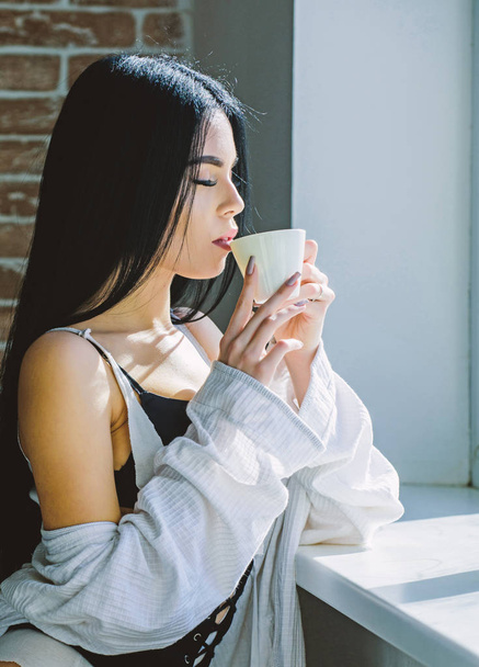 Drink well feel well. Pretty woman drinking healthy morning drink at window. Adorable girl holding cup with tasty coffee drink. Sexy woman enjoying her drink recipe - 写真・画像