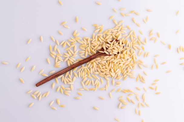 Makaron Orzo w drewnianej łyżce, wyizolowany na białym tle. Włoski makaron Orzo w kształcie ziaren ryżu - Zdjęcie, obraz