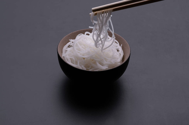 Тайский стиль приготовления рисовой лапши в миске с палочками для еды на черном фоне
 - Фото, изображение