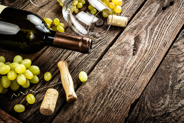 Weinhintergrund aus offener Weinflasche, Weinglas und Zweigen weißer Trauben auf dunklem, rustikalem Holzhintergrund mit Leerraum für einen Text - Foto, Bild