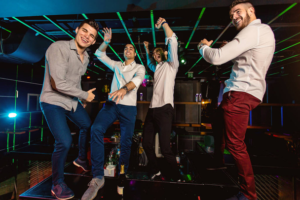 Grupo de amigos do sexo masculino sorridentes se divertindo no clube noturno
  - Foto, Imagem