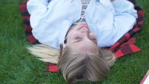 Happy student girl lying on the grass and listening to music. Top view portrait. - Metraje, vídeo