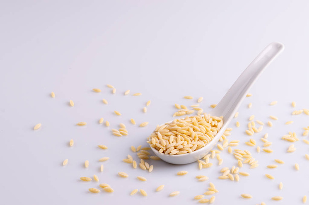 Orzo pasta in a white ceramic spoon, isolated on white background.  - Fotografie, Obrázek