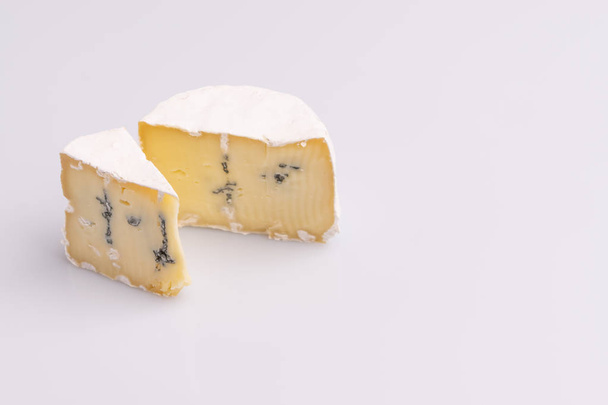Beyaz yüzeyli iki parça mavi peynir, beyaz arka plan, yumuşak ışık, stüdyo fotoğrafı, açı görünümü. Gorgonzola ve camembert / brie peynir karışımı - Fotoğraf, Görsel