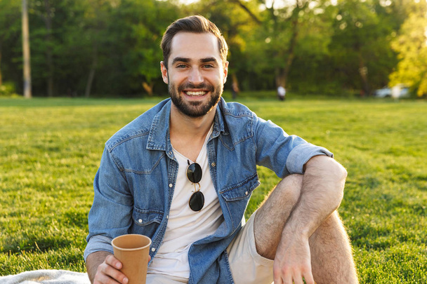 Cheerful young man having a picnic at the park - Zdjęcie, obraz