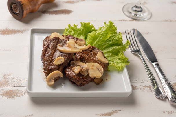 угол зрения филе миньон с грибным соусом, салатом, перцовый молоть на деревянном белом фоне
 - Фото, изображение