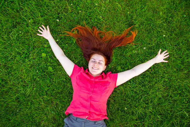 Portrait of a smiling red-haired young girl on green grass - Photo, Image