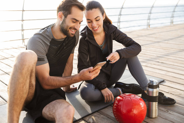Cheerful young sporty couple sitting on a fitness mat - Foto, immagini
