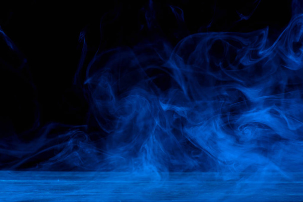 Концептуальне зображення синього диму ізольовано на темно-чорному фоні та дерев'яному столі
. - Фото, зображення