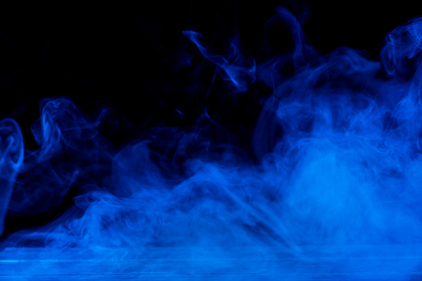 Imagen conceptual de humo azul aislado sobre fondo negro oscuro y mesa de madera
. - Foto, Imagen