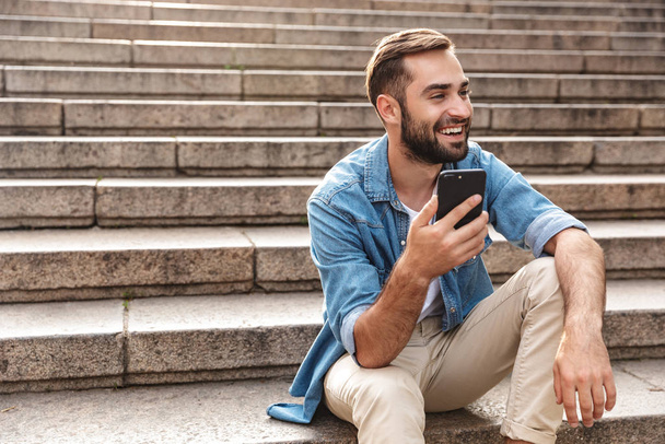 Smiling young man sitting on stairs outdoors - Photo, image