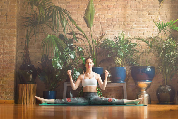 XoJeune femme pratiquant le yoga en studio. Assis sur le tapis vert
. - Photo, image