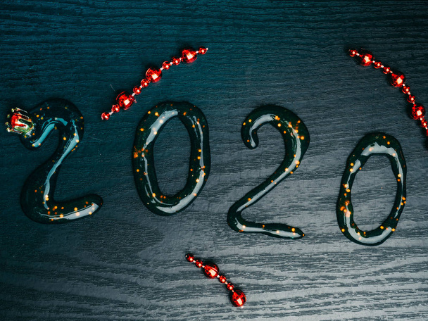 Grußkarte Frohes Neues Jahr 2020. Schöne Weitwinkel kreative Urlaub Web-Banner oder Werbetafel mit goldenen Pailletten, roten Girlanden, Inschrift aus Schleim 2020 geschrieben Wunderkerzen auf Holzgrund - Foto, Bild