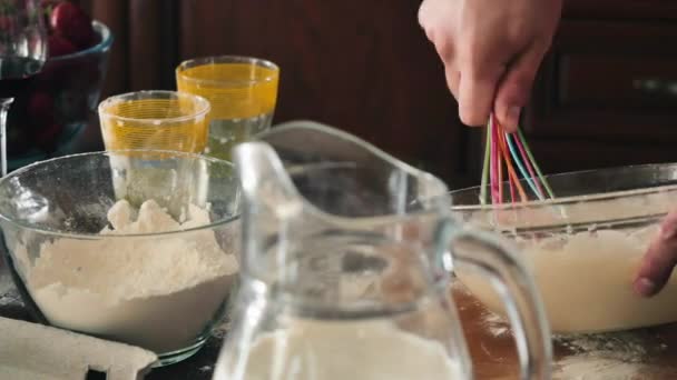 Close-up. Camera focuses on male hands with whisk. The man in apron is whisking the dough in a glass bowl for pancakes. The cook is moving the whisk with a circular movements inside a glass bowl. The guy dip finger inside a raw dough and taste it. - Metraje, vídeo