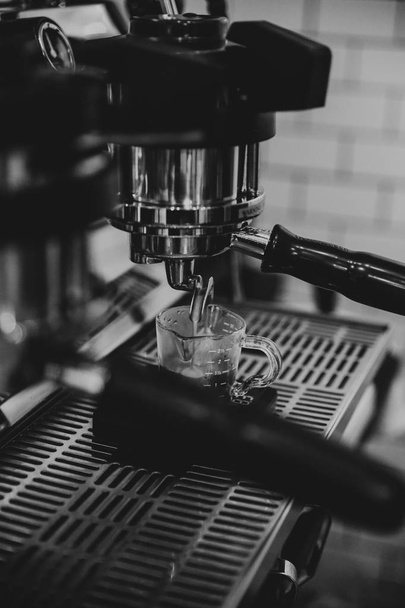Closeup of a metal coffee machine pouring coffee in a glass cup shot in black and white - Foto, Bild