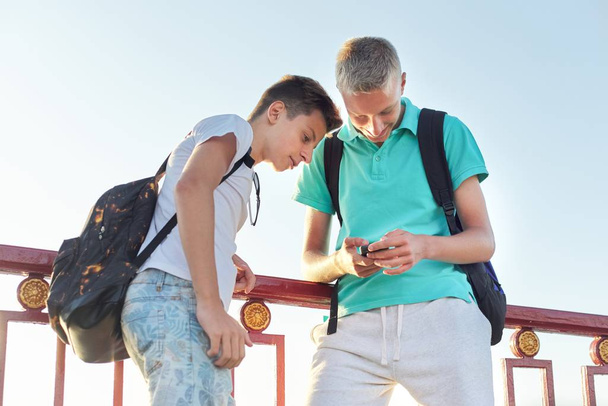 Two friends teenage boys using smartphone, talking and smiling - Fotó, kép