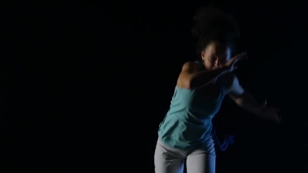 Lähikuva kihara nainen harjoitellaan capoeira pimeässä studiossa. Hidastus
 - Materiaali, video