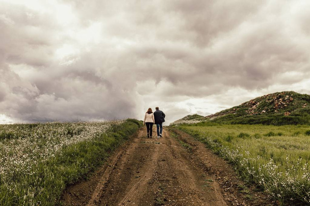 Aufnahme eines Mannes und einer Frau, die auf einem Pfad in einem Tal mit Blumen unter einem nebligen Himmel gehen - Foto, Bild
