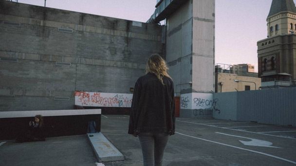 Female in a black coat walking on the roof of a parking garage with architecture in the background - Φωτογραφία, εικόνα