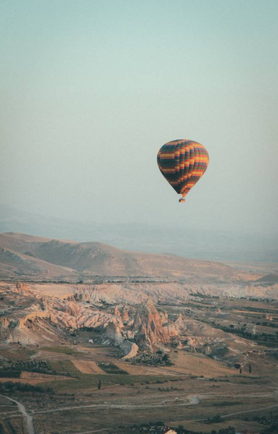 A long shot of a multi-colored hot air balloon floating in the sky high above mountains - Foto, Imagen