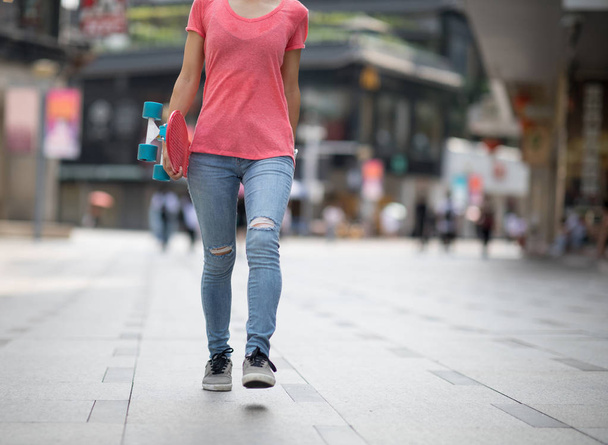 Woman walking with skateboard in hand at city - Fotó, kép