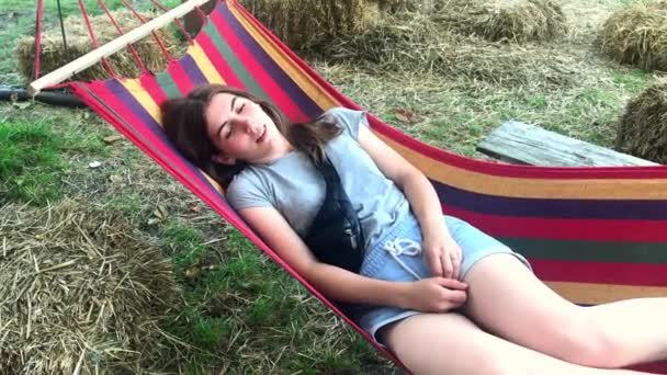 Piękna, śliczna młoda dziewczyna na letni dzień odpoczynku na kolorowym hamaku w parku lub na zewnątrz - Materiał filmowy, wideo