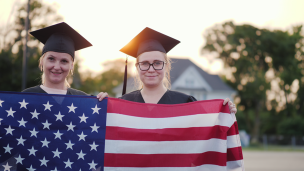 Dos graduados universitarios en batas y gorras con la bandera americana
 - Metraje, vídeo