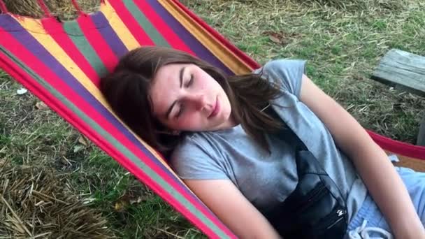 Piękna, śliczna młoda dziewczyna na letni dzień odpoczynku na kolorowym hamaku w parku lub na zewnątrz - Materiał filmowy, wideo