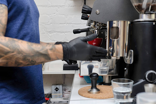 Hände eines professionellen Baristas stehen neben der großen Kaffeemaschine aus Metall - Foto, Bild