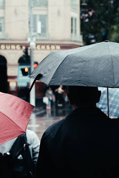 Osoba ve skupině lidí s černým deštníkem stojící v dešti - Fotografie, Obrázek