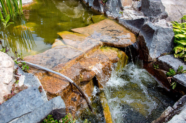 Stone waterfall in an artificial pond with flow water in the backyard on a sunny day. - Φωτογραφία, εικόνα
