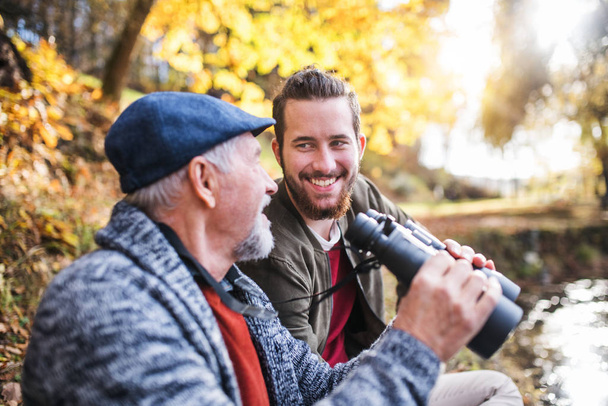 Senior father and his son with binoculars in nature, talking. - Photo, image