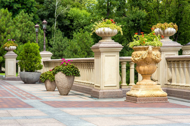 stone flowerpots at the railing with balustrades on the terrace with paving tiles and a garden of trees in the background. - 写真・画像