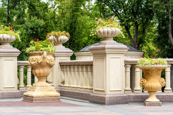 stone flowerpots at the railing with balustrades on the terrace and a garden of trees in the background. - Fotografie, Obrázek