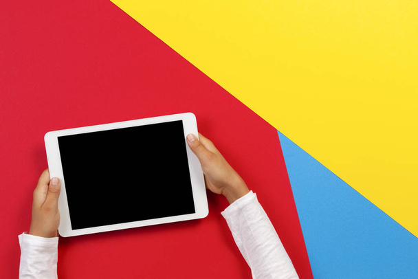 Kid hands with tablet computer on red, yellow and blue background - 写真・画像