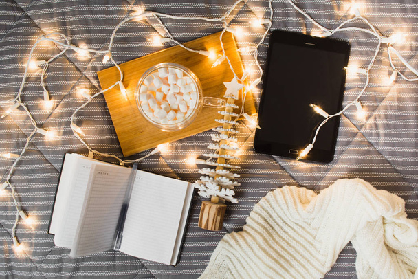 Christmas wish list or planning concept with tablet, note, marshmallow in mug and wooden fir tree. Cozy home. Freelancer's christmas morning. Flat lay - Zdjęcie, obraz