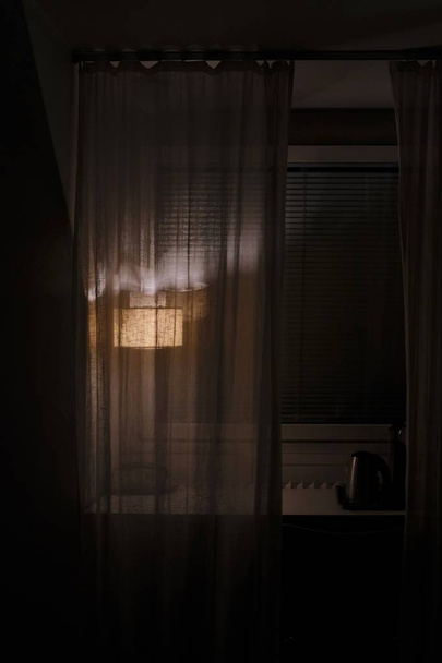 A dim lamp behind a transparent curtain on a windowsill - Zdjęcie, obraz