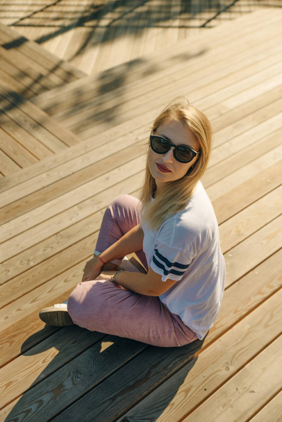 Jonge hippe vrouw zittend op de houten vloer. Draag jeans en een wit t-shirt - Foto, afbeelding