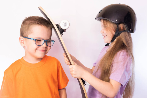 Маленька дівчинка в захисному шоломі потрапляє в голову смішного хлопчика зі скейтбордом, на світлому тлі
 - Фото, зображення