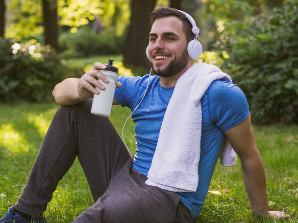 Handsome man with headphones  drinking water and resting after exercise in the park. - Φωτογραφία, εικόνα