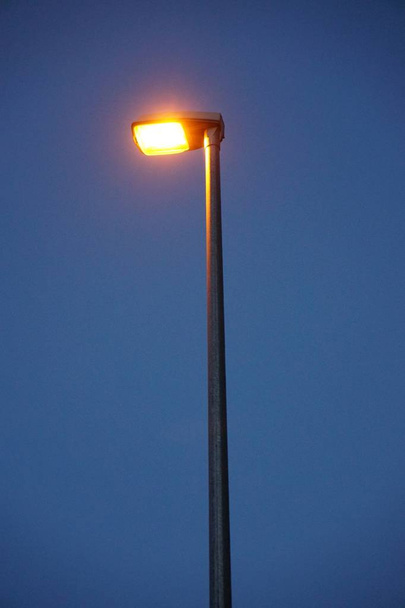 Vertical shot of a metal illuminated street lamp on a dark blue background - Фото, зображення