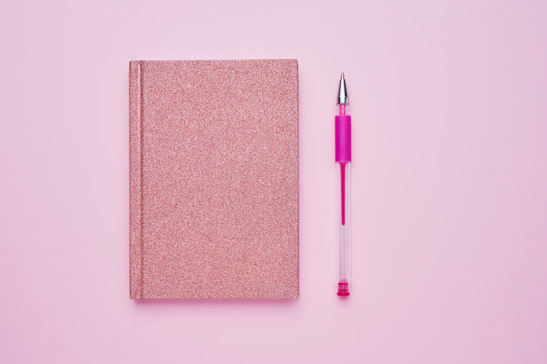 パステルピンクの背景にペンを持つピンクのメモ帳。学校の概念に戻る。コピースペース、トップビュー. - 写真・画像