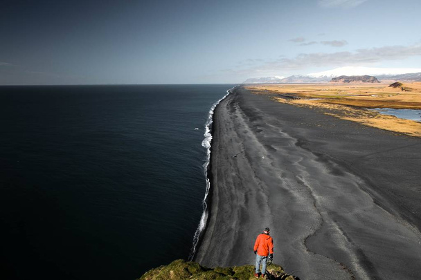 Beautiful wide shot of a person standing on a rock near a sea and seashore - Foto, Bild