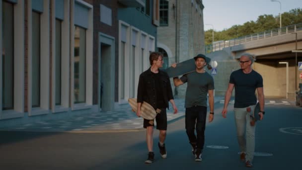 Трое крутых парней разговаривают, веселятся во время прогулок и переносят скейтборды. Стильные молодые друзья по улице. На заднем плане Модный современный район хипстеров
 - Кадры, видео